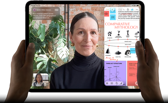 iPad Pro, pohled zepředu, orientace na šířku, vesmírně černá barva, zaoblené rohy, černý rámeček displeje, ruce drží levou a pravou stranu, na displeji se zobrazuje FaceTime konverzace překládaná v reálném čase a vzdělávací aplikace s prezentací na téma komparativní mytologie, textem, diagramy a ručně psanými poznámkami