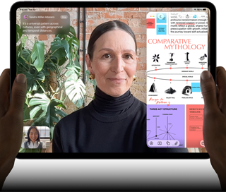 iPad Pro, pohled zepředu, orientace na šířku, vesmírně černá barva, zaoblené rohy, černý rámeček displeje, ruce drží levou a pravou stranu, na displeji se zobrazuje FaceTime konverzace překládaná v reálném čase a vzdělávací aplikace s prezentací na téma komparativní mytologie, textem, diagramy a ručně psanými poznámkami