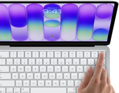MacBook Neo, stříbrná barva, zobrazuje se přihlašovací obrazovka, něčí prst na snímači Touch ID v pravém horním rohu klávesnice